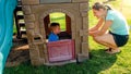 Portrait of happy young mother looking at her laughing toddler boy playing in toy house at playground Royalty Free Stock Photo