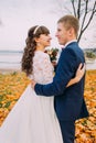 Portrait of happy young newly married couple posing on autumn lakeshore full orange leaves Royalty Free Stock Photo