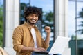 Portrait of a happy young Nigerian man sitting on a bench outside with a laptop, smiling at the camera and showing a Royalty Free Stock Photo