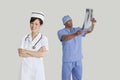 Portrait of happy young nurse with male surgeon examining x-ray report over gray background Royalty Free Stock Photo