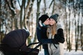 Portrait of a happy young parents stand and kissing with a stroller baby in a winter park. headshot, half length. Close up. Family Royalty Free Stock Photo