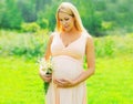 Portrait of happy young pregnant woman with flowers in sunny summer day Royalty Free Stock Photo