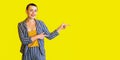 Portrait of happy young short hair beautiful woman in yellow shirt and striped suit standing pointing at copyspace on yellow Royalty Free Stock Photo