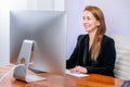 Portrait of happy young successful businesswoman at office. She sits at the table, looks at the display and laugh, office work. Bl