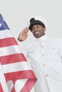 Portrait of a happy young US Navy officer saluting American flag over gray background Royalty Free Stock Photo