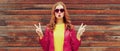 Portrait of happy young woman blowing her lips with lipstick sending kiss wearing red leather jacket, heart shaped sunglasses in Royalty Free Stock Photo