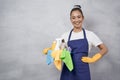 Portrait of a happy young woman, cleaning lady in uniform with bucket of cleaning supplies standing against grey wall Royalty Free Stock Photo
