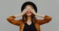happy young woman covering her eyes with her hands wearing a black round hat over gray background Royalty Free Stock Photo