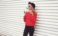 Portrait happy young woman drinks coffee and holding sweet donut on city street white wall