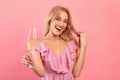 Portrait of happy young woman holding glass of sparkly champagne, smiling and looking at camera on pink background Royalty Free Stock Photo