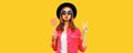 Portrait of happy young woman holding lollipop and blowing her lips sends air kiss wearing pink jacket, black round hat on yellow Royalty Free Stock Photo