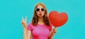 Portrait of happy young woman holding red heart shaped balloon and blowing lips sending sweet air kiss on blue background Royalty Free Stock Photo
