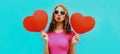 Portrait of happy young woman holding red heart shaped balloon and blowing lips sending sweet air kiss on blue background Royalty Free Stock Photo