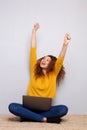 Happy young woman laughing with laptop and arms raised against gray background Royalty Free Stock Photo