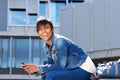 Happy young woman with mobile phone sitting outside and laughing Royalty Free Stock Photo