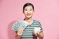 Portrait of happy young woman with money and piggy bank on pinkbackground