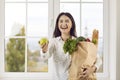Portrait of happy young woman with paper grocery bag in her hands in which fresh organic food. Royalty Free Stock Photo