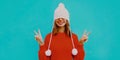 Happy young woman pulled hat over her eyes wearing white hat with pom pom, red knitted sweater on a blue background