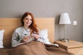 Portrait of happy young woman shopping online with credit card and smartphone sitting in bed at home, looking at camera. Royalty Free Stock Photo