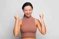 Portrait of happy young woman in short turtleneck exults pumping fists ecstatic celebrates success gesturing YES against gray Royalty Free Stock Photo