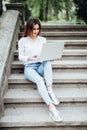 Portrait of a happy young woman sitting on the city stairs and using laptop computer outdoors Royalty Free Stock Photo