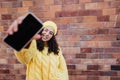 Portrait of happy young woman with smartphone in front of brick wall in city street, looking at camera. Royalty Free Stock Photo