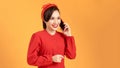 Portrait of a happy young woman wearing red dress standing isolated over yellow background, talking on mobile phone Royalty Free Stock Photo