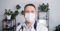 Portrait of healthcare professional. Positive Caucasian male dentist doctor in lab coat, face mask smiles at camera.