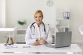 Friendly young woman, working as doctor, sitting at desk in hospital office, smiling and looking at camera. Royalty Free Stock Photo