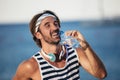 Healthy athletic man with fit body holding bottle of refreshing water, resting after workout or running at beach Royalty Free Stock Photo