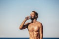 Healthy athletic man with fit body holding bottle of refreshing water, resting after workout or running at beach Royalty Free Stock Photo