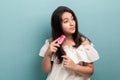 Portrait of healthy beautiful teenager brunette girl in white dress standing and combing brunette hair with pink hairbrush.