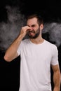 Man in white t-shirt on black background closes nose