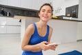 Portrait of healthy young sporswoman, smiling and holding smartphone, doing workout training at home in her house