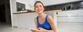 Portrait of healthy young sporswoman, smiling and holding smartphone, doing workout training at home in her house