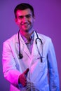 Portrait of a hero in a white coat. Cheerful smiling young doctor with stethoscope in medical hospital standing on blue Royalty Free Stock Photo