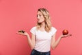 Portrait of hesitating blond woman 20s wearing casual t-shirt holding sweet donut and fresh healthy apple Royalty Free Stock Photo