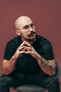 Portrait of hipster bald bearded man with moustache in glasses who sitting on chair in studio Royalty Free Stock Photo