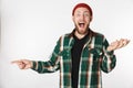 Portrait of hipster guy wearing hat and plaid shirt laughing and pointing finger aside, while standing isolated over white Royalty Free Stock Photo