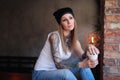 Portrait of a hipster tattoed girl holds takeaway coffee and looks out the window while sitting on the table in a room Royalty Free Stock Photo