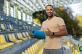 Portrait of hispanic male fitness trainer at sports stadium, athlete with yoga mat smiling and looking at camera Royalty Free Stock Photo