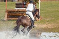 Portrait of horse and rider galloping in water during eventing competition
