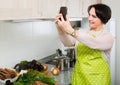 Portrait of housewife in apron making selfie in domestic kitchen Royalty Free Stock Photo