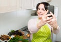 Portrait of housewife in apron making selfie in domestic kitchen Royalty Free Stock Photo