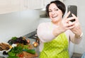 Portrait of housewife in apron making selfie in domestic kitchen Royalty Free Stock Photo