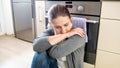 Portrait of young housewife feeling exhausted and upset sitting on floor at kitchen