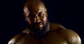 Portrait of a huge bald bearded man with bronze skin on a black background. he stares at the camera, moving his muscles