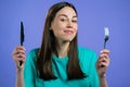 Portrait of hungry woman with fork and knife. Lady waiting for serving dinner dishes with cutlery on violet studio Royalty Free Stock Photo