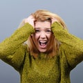 Portrait of a hysterical woman pulling hair out against gray background