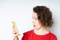 Portrait if a shocked young girl in a red sweater looking at mobile phone isolated